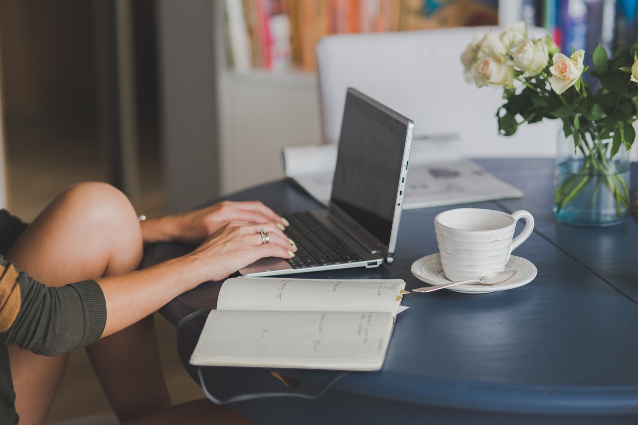 woman seated at a table, working on a laptop with a cup of coffee beside her