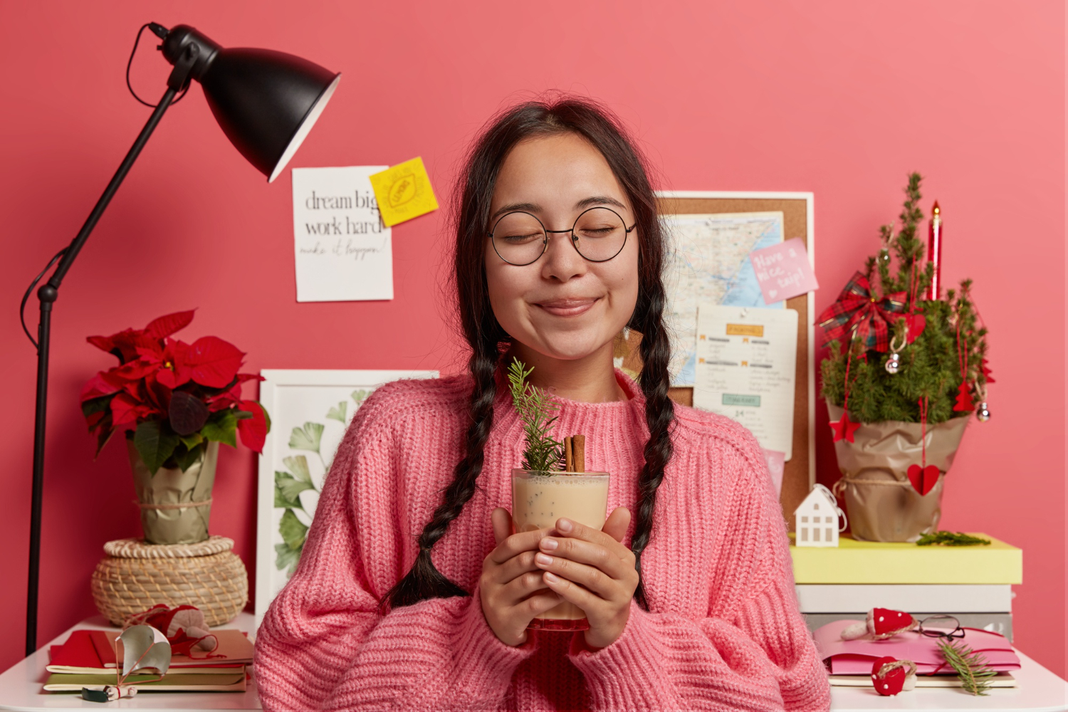 A girl with glasses stands holding a potted plant in front of a bright pink backdrop